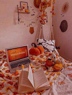 an open book sitting on top of a bed next to two pumpkins and a laptop