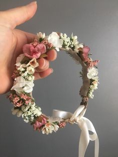 a hand is holding a flower wreath with white and pink flowers on the inside of it