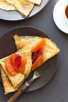 two plates with pancakes and orange slices on them next to a cup of tea or coffee