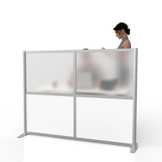 a woman is sitting at a desk in front of a white screen with glass doors