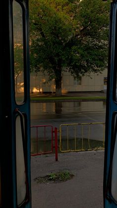 an open bus door with trees in the background and water on the street behind it