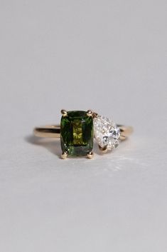 an emerald and diamond ring with three pear shaped diamonds on the band, set in yellow gold