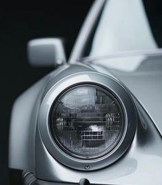 the front end of a silver sports car with its lights on and headlight showing