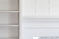 an empty room with white walls and shelving unit in the corner, next to a marble fire place