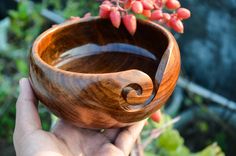 a hand holding a wooden bowl with red flowers in the backgroung area