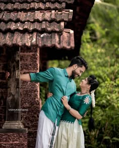 a man and woman standing next to each other in front of a building with roof tiles