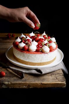 someone is decorating a cake with strawberries and whipped cream on the top layer