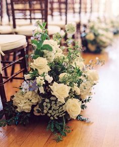 white flowers and greenery sit on the floor in front of rows of wooden chairs