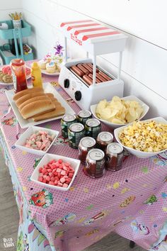 a table topped with lots of food on top of a pink tablecloth covered table