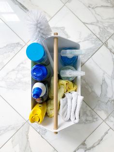 an open bin filled with cleaning supplies on top of a white tiled floor next to a wooden stick