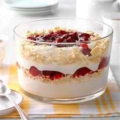 a dessert with strawberries and cream in a glass dish on a yellow tablecloth