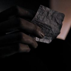 a person's hand holding a piece of paper in the dark with their fingers