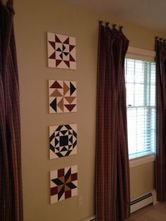 three quilts are hanging on the wall next to two windows with matching drapes