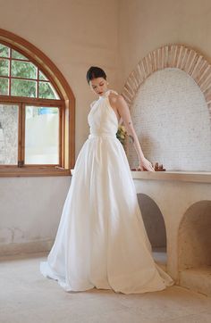 a woman in a white dress standing by a window