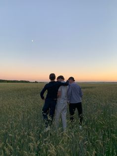 three young men standing in a field at sunset