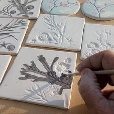 a person is drawing on some tiles with a pencil and watercolors in front of them