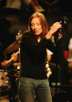 a woman standing in front of a microphone with her hand up to the side while singing