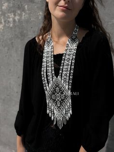 a woman wearing a black shirt and some necklaces on her neck is standing in front of a concrete wall