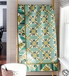 a green and white quilt sitting on top of a wooden stand next to a window