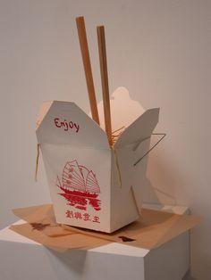 a box with chopsticks sticking out of it sitting on top of a block of cardboard