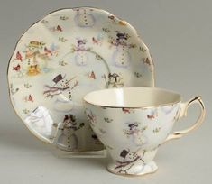 a white cup and saucer with snowmen on the side, sitting next to each other