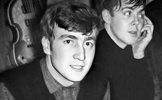 two young men sitting next to each other with guitars in the back ground behind them