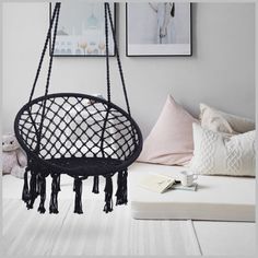 a black hanging chair with tassels in a white room next to pillows and pictures on the wall