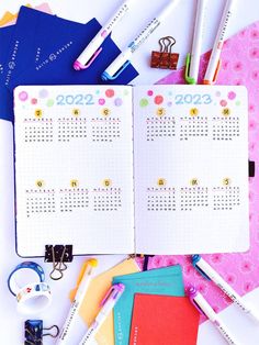 an open planner book sitting on top of a desk next to office supplies and pens