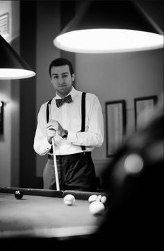 a man standing in front of a pool table holding a cue and wearing a bow tie