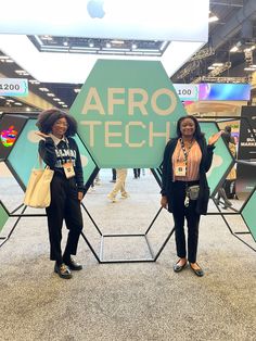 two women standing next to each other in front of a sign that says afro tech