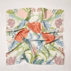 an orange and pink flowered scarf on top of a white surface with green leaves