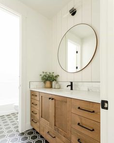 a bathroom with a large round mirror above the sink and wooden cabinetry, along with black and white patterned floor tiles