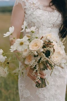 a woman in a wedding dress holding a bouquet of white and beige flowers on her left hand