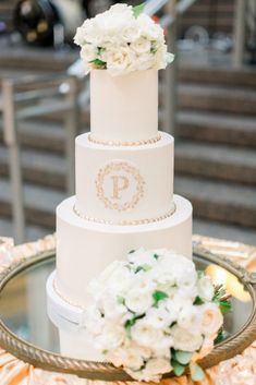 a three tiered wedding cake with white flowers on the top and monogrammed initials