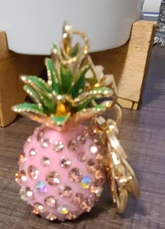 a pink pineapple shaped object with gold trimmings on a wooden table next to a white bowl