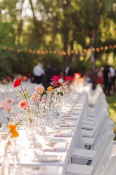 a long table is set up with white chairs and flowers in vases on the tables