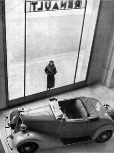 an old car is parked in front of a window with a woman standing next to it