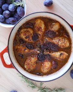 a pot filled with chicken and olives next to blueberries on a wooden table