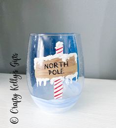 a hand painted wine glass with the words north pole on it and a wooden sign