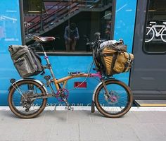 a bicycle parked next to a blue train with luggage on the front and back rack