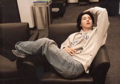 a young man sitting on top of a black leather chair in an office building with his arms behind his head