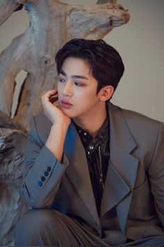 a young man sitting on top of a wooden bench next to a tree trunk with his hand under his chin