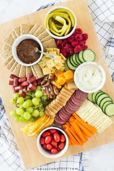 a platter with crackers, grapes, cucumbers, and other snacks