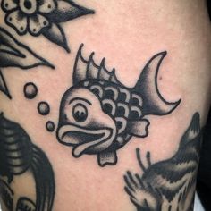 a black and white photo of a fish on the thigh with other tattoos around it