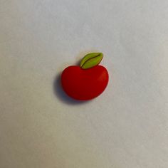 a red apple with a green leaf on it's tip sitting on a white surface