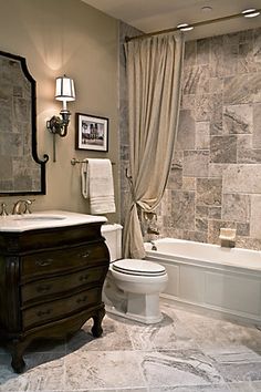 a white toilet sitting next to a bath tub under a bathroom mirror above a sink