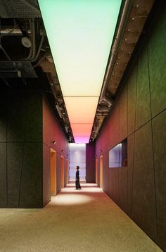 a person walking down a long hallway with green and pink lighting on either side of it