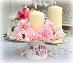 two candles are on a plate with pink flowers and pearls around the edge, along with other decorative items