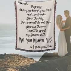 a man and woman standing next to each other on top of a rock near the ocean