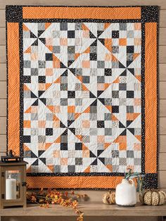 an orange and black quilt hanging on the wall next to a small table with pumpkins